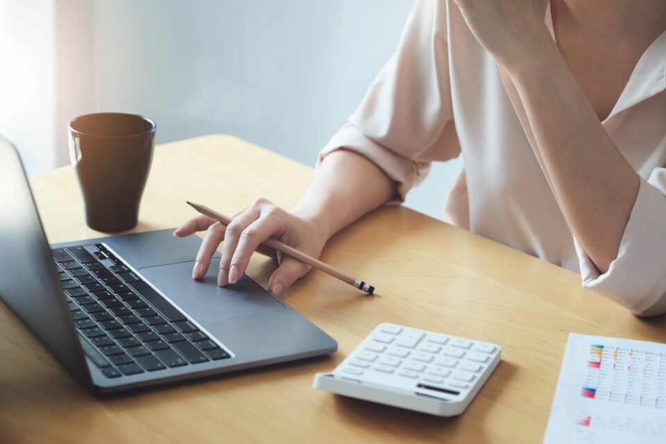 Une femme est assise à son bureau, entourée de documents et son ordinateur, illustrant la réussite de la gestion du Total Cost of Mobility (TCM) dans l'entreprise. Cette image symbolise l'efficacité de l'optimisation financière et la performance de la mobilité professionnelle.